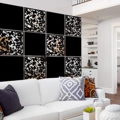 a living room filled with white furniture and lots of black and gold wall art on the walls