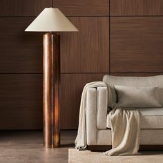 a white couch sitting next to a lamp on top of a hard wood floor in front of a wooden wall