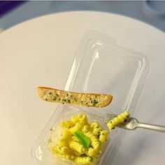 a plastic container filled with macaroni and cheese on top of a white table