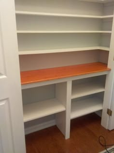 an empty room with white shelves and wood flooring in the corner, next to a door