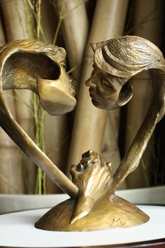 a bronze statue of a boy and girl holding each other's hands in front of bamboo trees