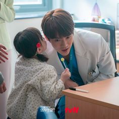 a young child is sitting at a desk with an adult in front of him and holding a pen