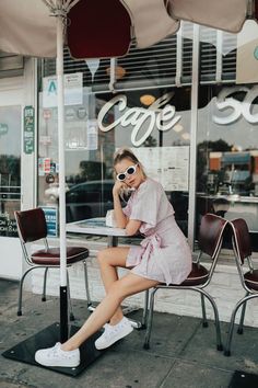 a woman sitting at a table talking on her cell phone in front of a cafe