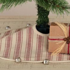 a present wrapped in brown paper and tied with twine, sitting on a striped pillow next to a pine tree