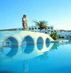 a woman standing on top of a bridge over a pool