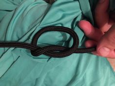 a person holding a black rope on top of a blue sheeted bed with their hand