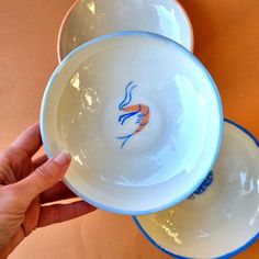 two white and blue bowls with fish designs on them are being held by someone's hand