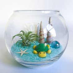 a fish bowl filled with blue sand and sea shells on top of a white table