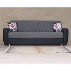 a couch with two pillows on top of it next to a table and chair in front of a wall