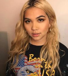 a woman with long blonde hair and an american flag t - shirt is looking at the camera