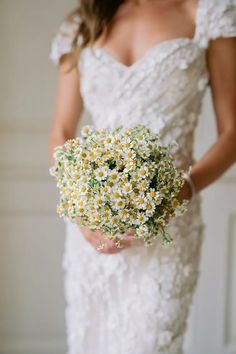 a woman in a wedding dress holding a bouquet of daisies and baby's breath