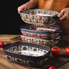 a person holding a bowl in front of four bowls with tomatoes on the table behind them