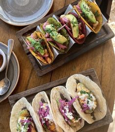 four tacos on wooden trays sitting on a table next to cups and saucers