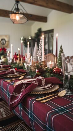 the table is set for christmas dinner with candles and plaid napkins on it, along with other holiday decorations