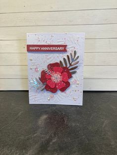 a happy anniversary card with a red flower and leaves on the front, sitting on a table