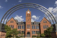 the entrance to an old brick school with a clock tower in the center and arches over it