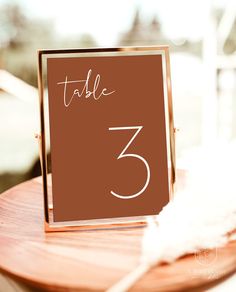 a table number is placed on top of a wooden stand with a feather in the foreground