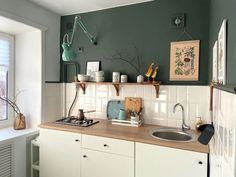 a kitchen with green walls and white cupboards, wooden counter tops, and an open window