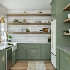 a kitchen with green cabinets and white subway backsplashes, wood flooring and open shelving