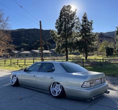 a silver car parked in a parking lot next to a fence and trees with mountains in the background