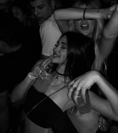 several people are dancing and having drinks at a club or bar, one woman is drinking from a wine glass while the other has her arm around her neck