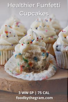 some cupcakes with white frosting and sprinkles on top are sitting on a wooden board