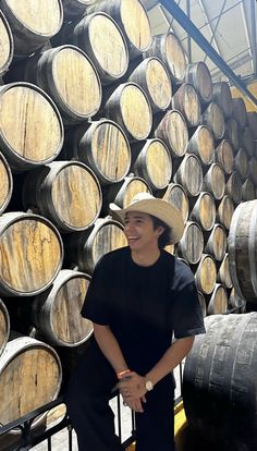 a man in a hat standing next to some wooden barrels with wine casks behind him