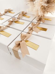 several white boxes with brown bows and gold tags tied around the top, on a table