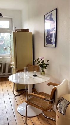 a table with two chairs and a refrigerator in a room that has wood floors on the floor