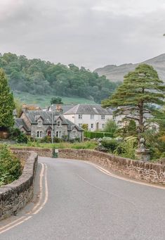 an empty street with houses in the background and trees on both sides, near a stone wall