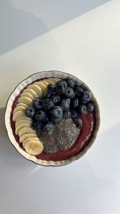 a bowl filled with blueberries and bananas on top of a white table next to a cup of coffee