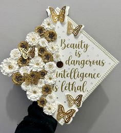 a graduation cap with flowers and butterflies on the top is decorated in gold, white and black