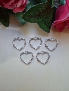 four silver heart shaped rings sitting on top of a table next to pink flowers and greenery