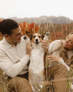 a man and woman petting a small dog in the middle of some tall grass