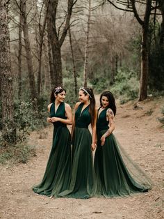 three bridesmaids in green dresses standing together on a dirt path surrounded by trees