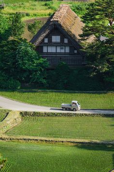 a truck is driving down the road in front of a house with a thatched roof