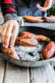 a person is frying hot dogs in a pan on a table with other food