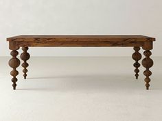 an old wooden table with turned legs on a plain white flooring area in front of a wall