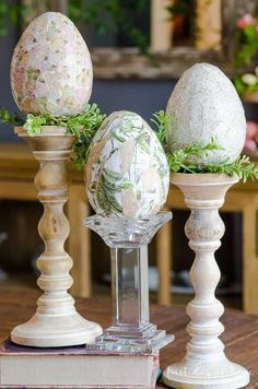 three decorative easter eggs sitting on top of each other next to an egg holder with greenery