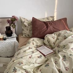 an unmade bed with flowers on it next to a night stand and nightstands