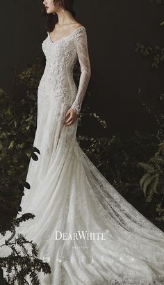 a woman in a white wedding dress standing next to some bushes and trees with her hands on her hips