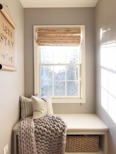 a white bench sitting under a window next to a basket filled with pillows and blankets