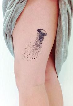 a small jellyfish tattoo on the left thigh and right leg, with tiny dots coming out of it