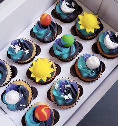 twelve cupcakes with blue frosting and stars on them in a white box