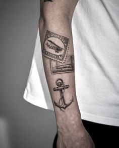 a man's arm with an anchor and postage stamp tattoo on the left forearm