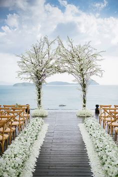 an outdoor ceremony set up with wooden chairs and flowers on the aisle, overlooking the water