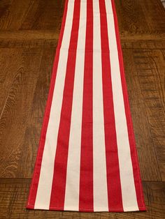 a red and white striped table runner on a wooden floor with an orange vase in the background