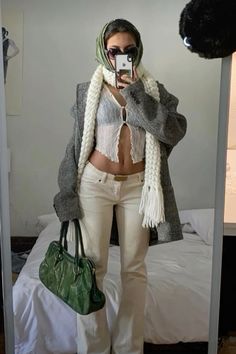 a woman taking a selfie while wearing white pants and a gray jacket with a green handbag