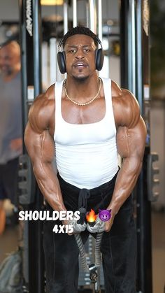 a man with headphones on standing in front of a gym machine and looking at the camera