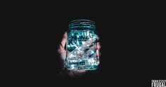 a person holding a mason jar with lights in it's hands, against a black background